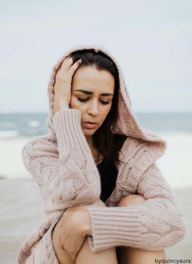 woman sitting in front of a beach wearing oversized chunky knit sweater