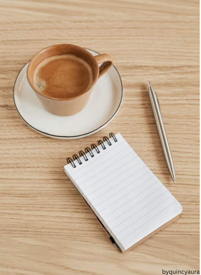 An image of a journal, beside a cup of coffee on a table.