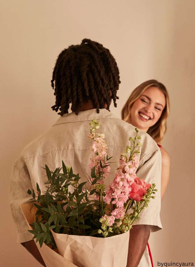 A couple smiling as one surprises the other with flowers