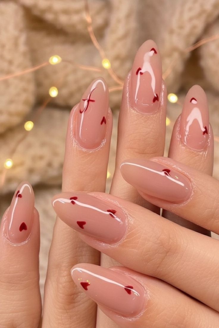 Short almond or square nails with a sheer pink base and small red hearts at the tips.