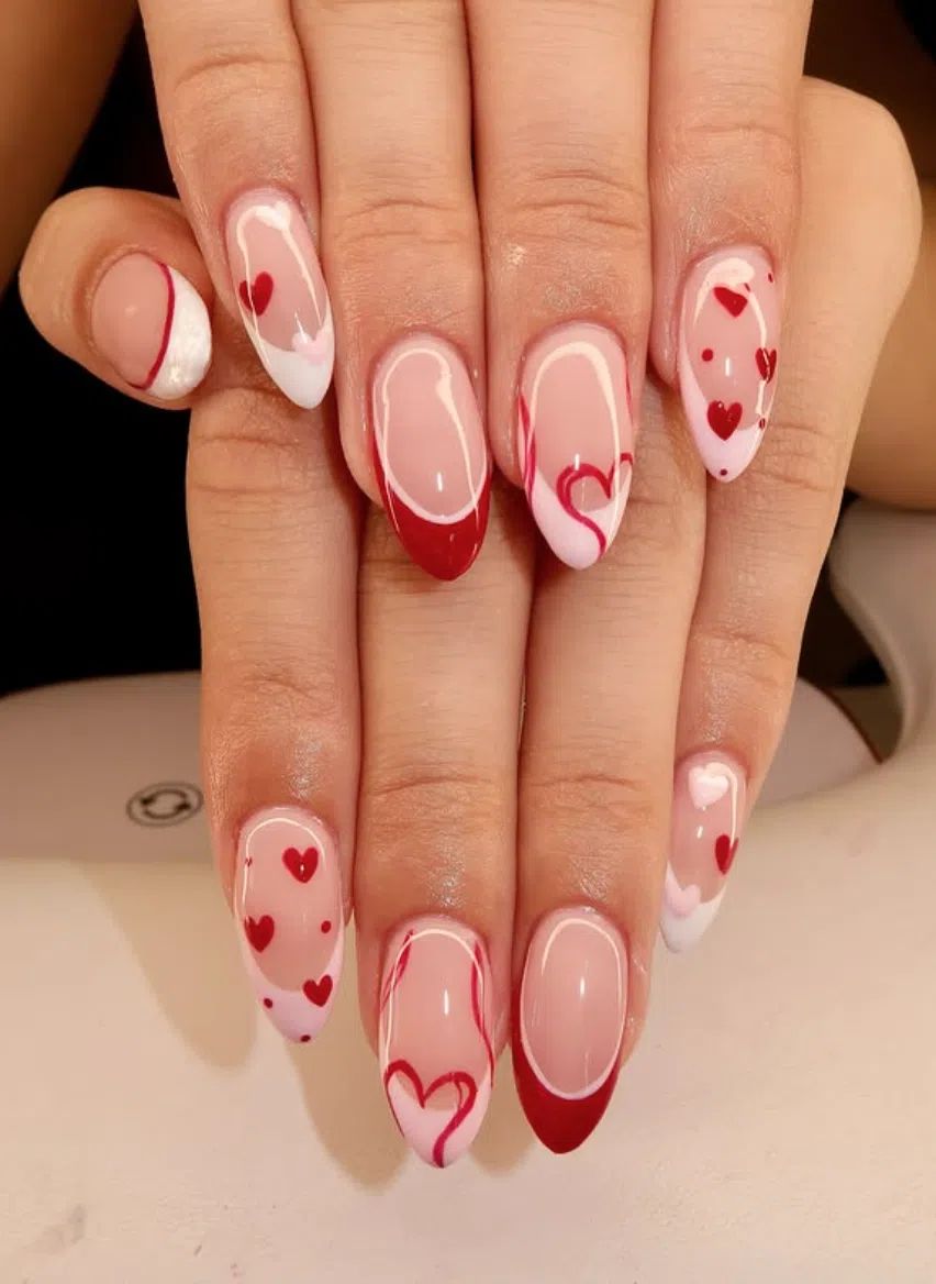 medium nails with a nude base and scattered tiny heart confetti in pink and red.