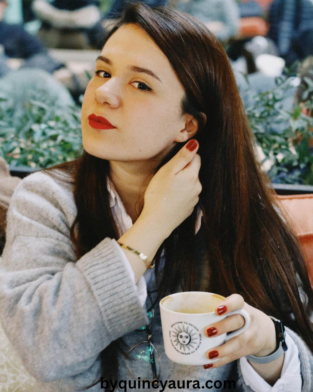 A woman styled in jeans and a soft knit top, sitting in a café with a coffee cup.