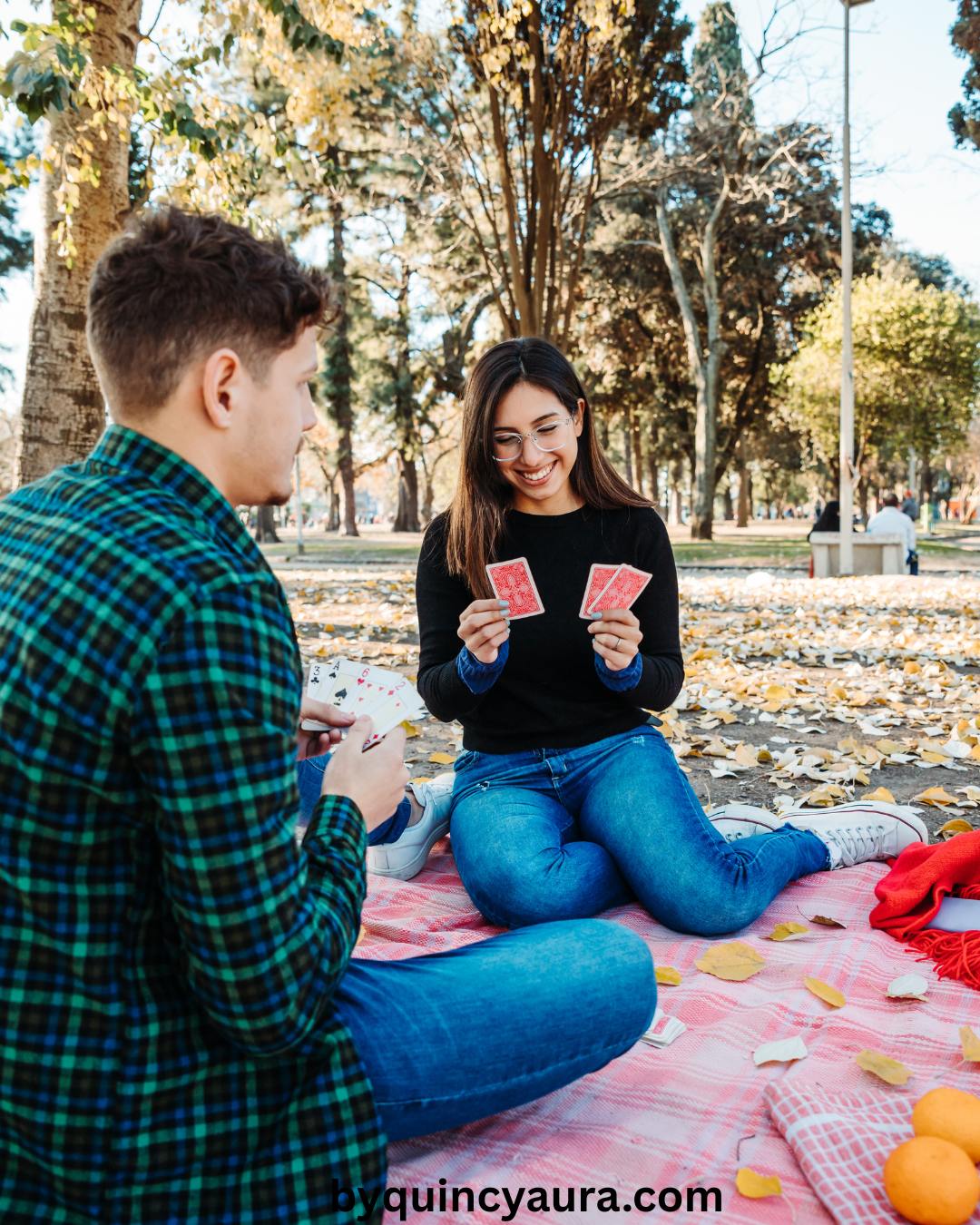 A couple playing cards or writing in a small notebook on a picnic blanket.