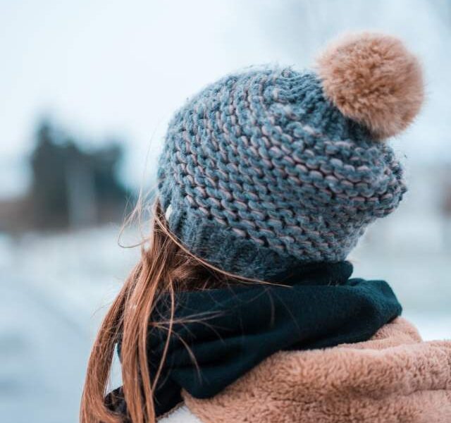 A woman wearing a cozy scarf and beanie, showing healthy hair and smooth skin.