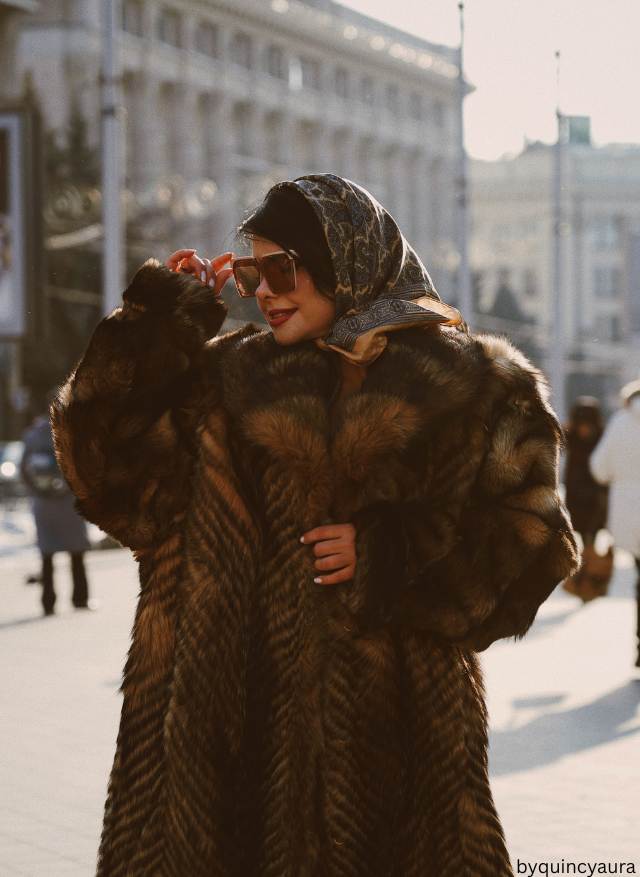 A woman wearing a summer dress styled with winter boots, tights, and a coat.