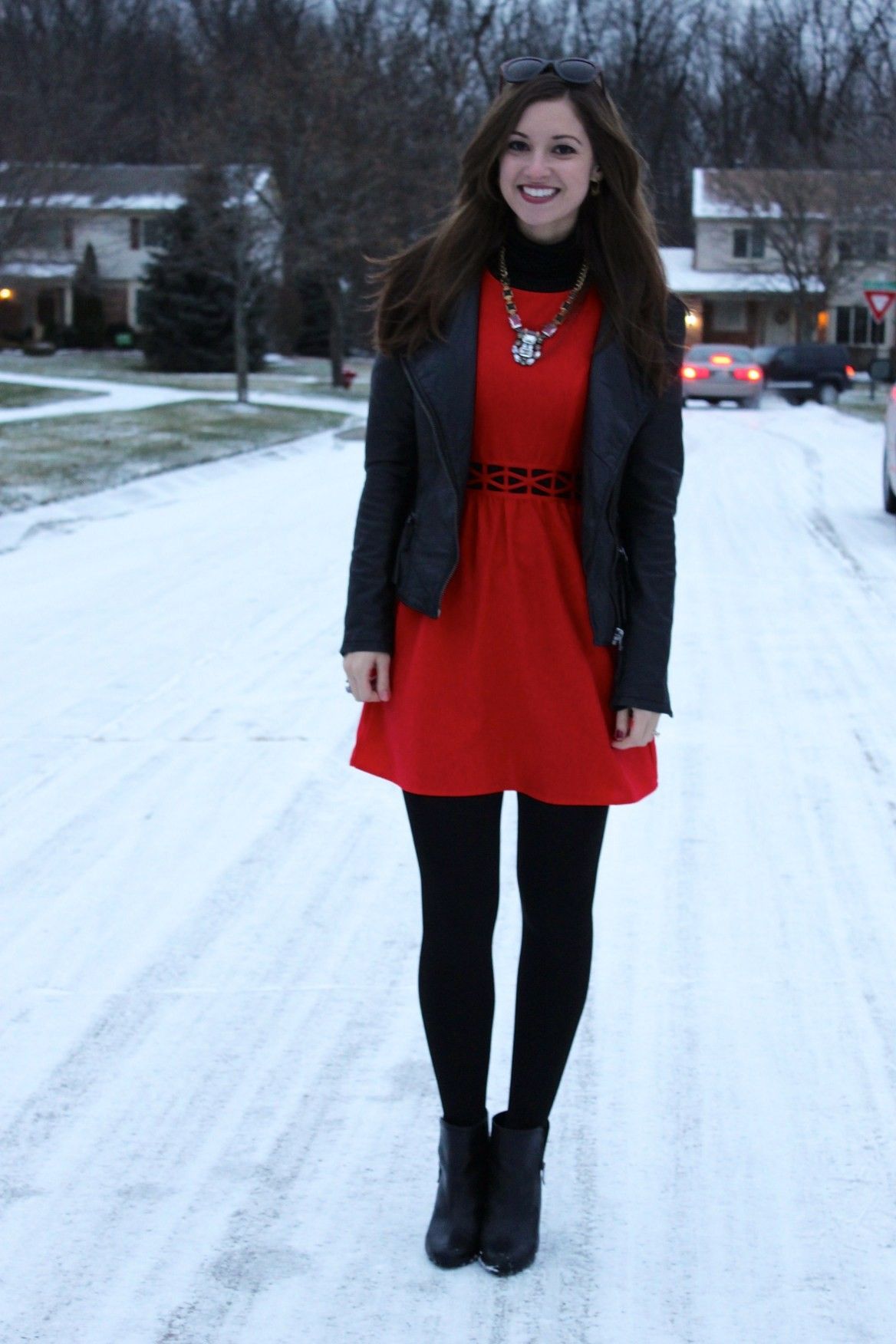 A woman wearing a red dress layered over a black turtleneck, styled with black boots or loafers.