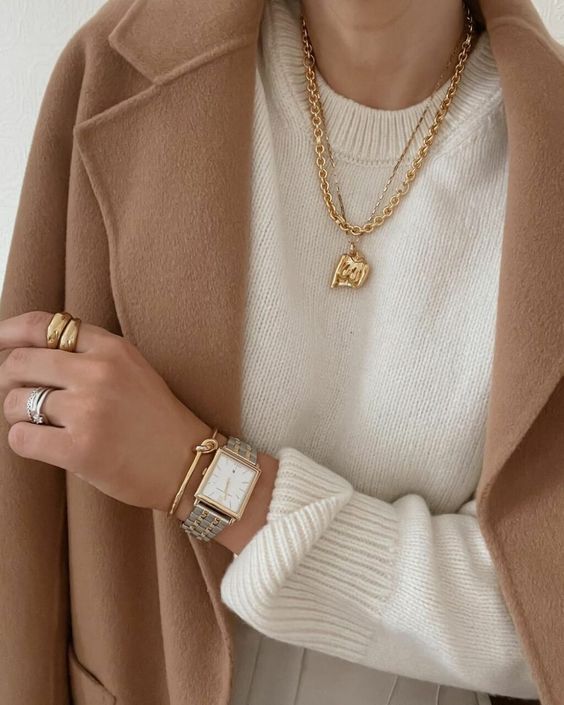 Layered gold necklaces over a neutral turtleneck sweater.